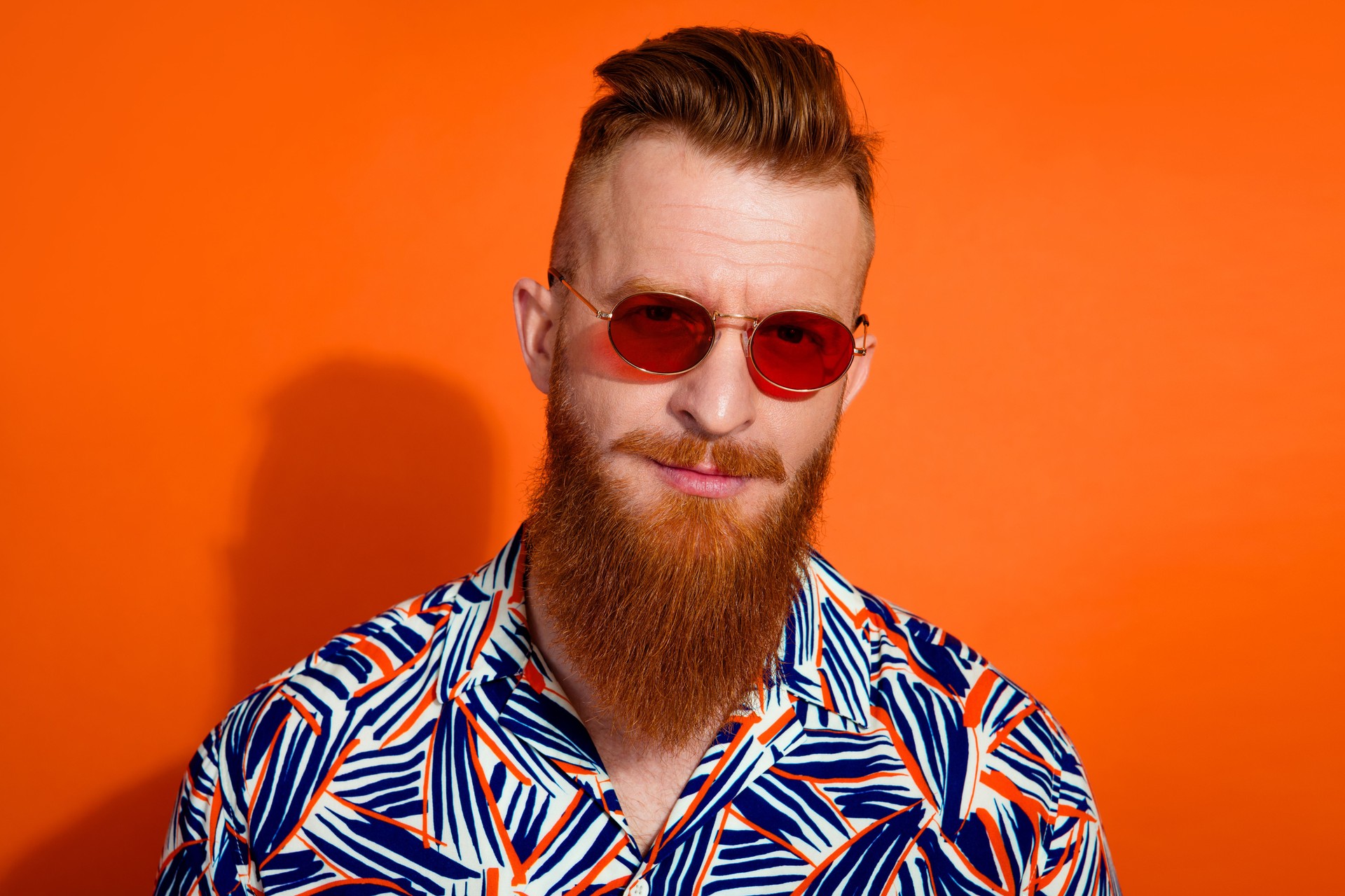 Photo of virile guy with red beard trendy heaicut wear stylish shirt in sunglass look at you isolated on vibrant orange color background